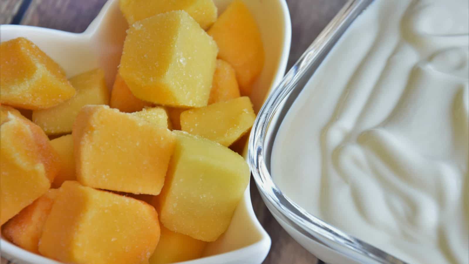 Frozen mango chunks beside a bowl of yogurt.