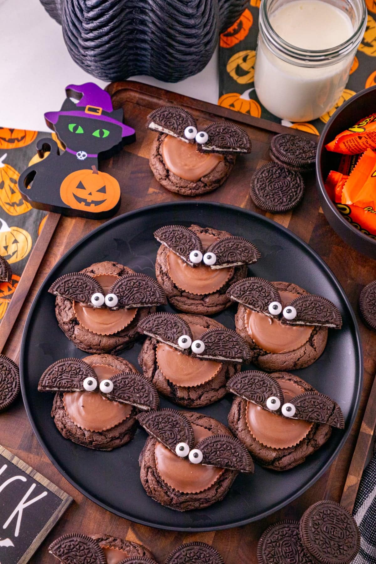 Oreo bat cookies with Reese’s peanut butter cups, Oreo wings, and candy eyes arranged on a black plate with Halloween decorations.