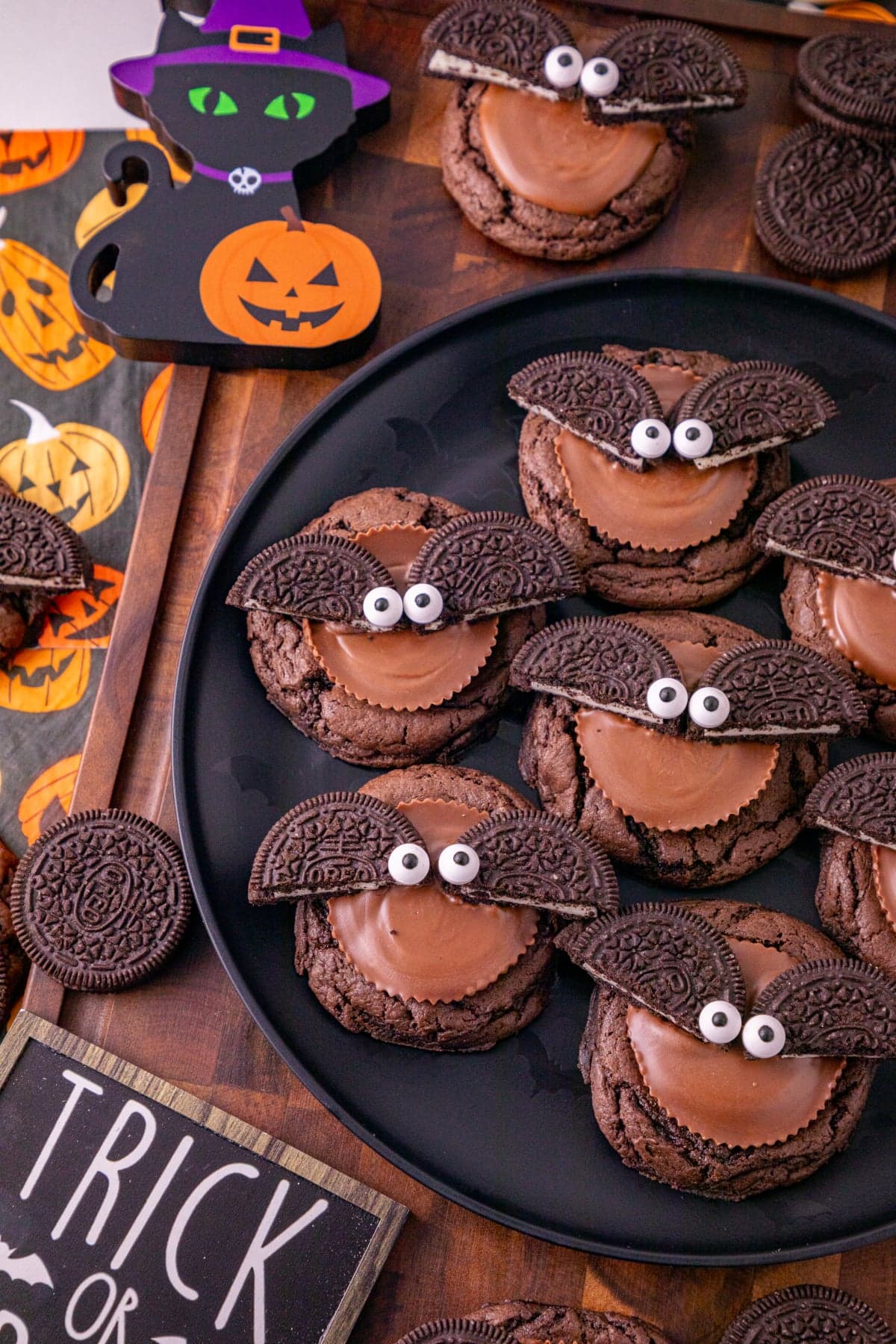 Close-up of Oreo bat cookies topped with Reese’s peanut butter cups and candy eyes on a Halloween dessert table.