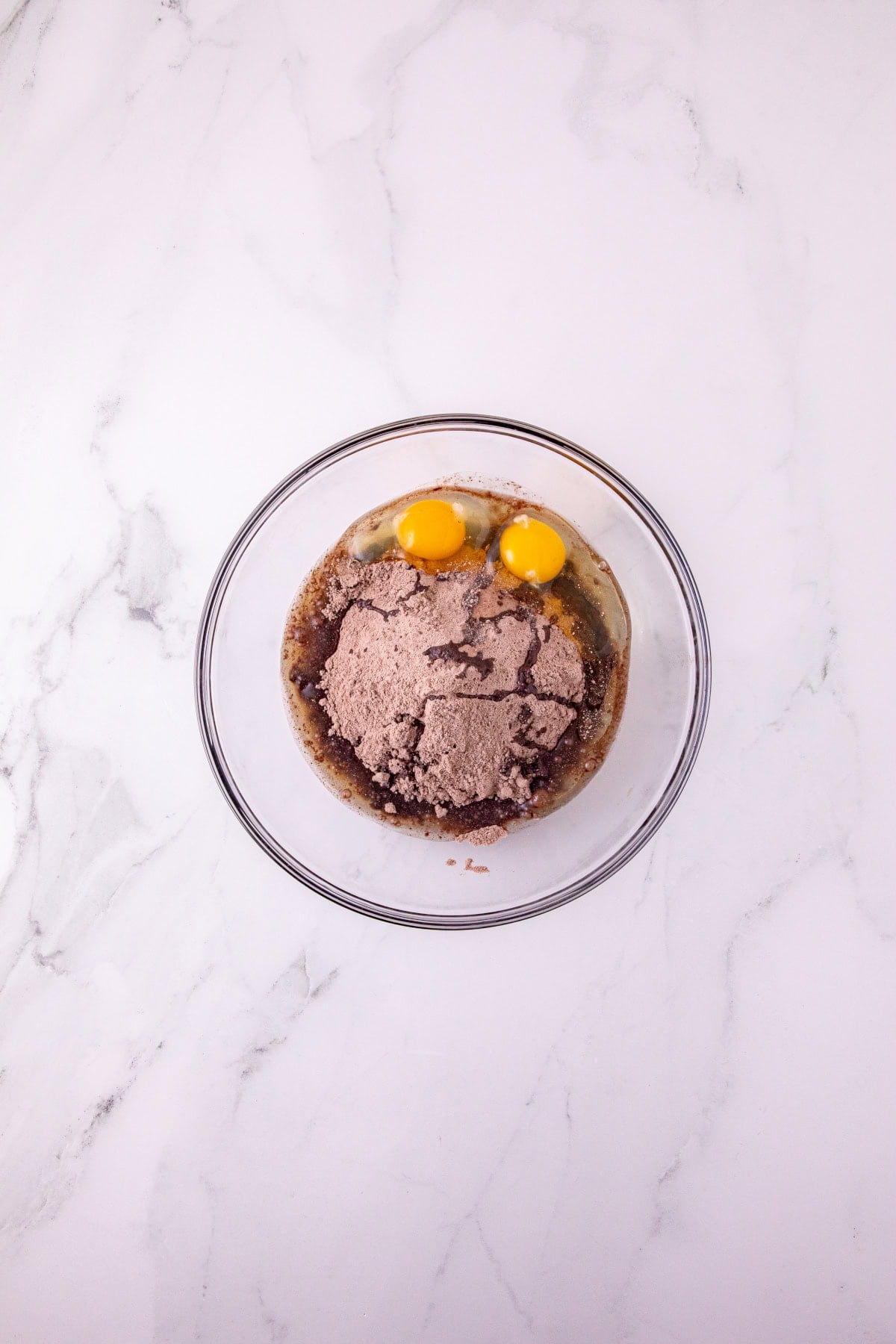 Chocolate cake mix, eggs, and oil combined in a glass mixing bowl.