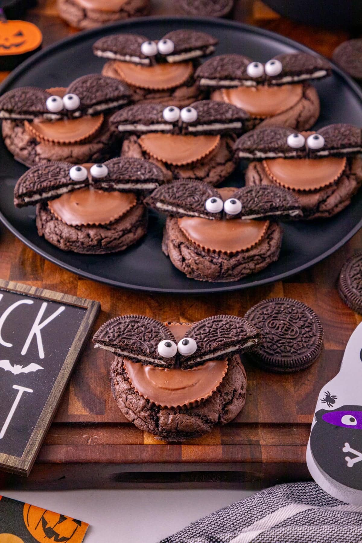 Oreo bat cookies arranged on a black plate with Reese’s peanut butter cups, Oreos, and Halloween decorations.