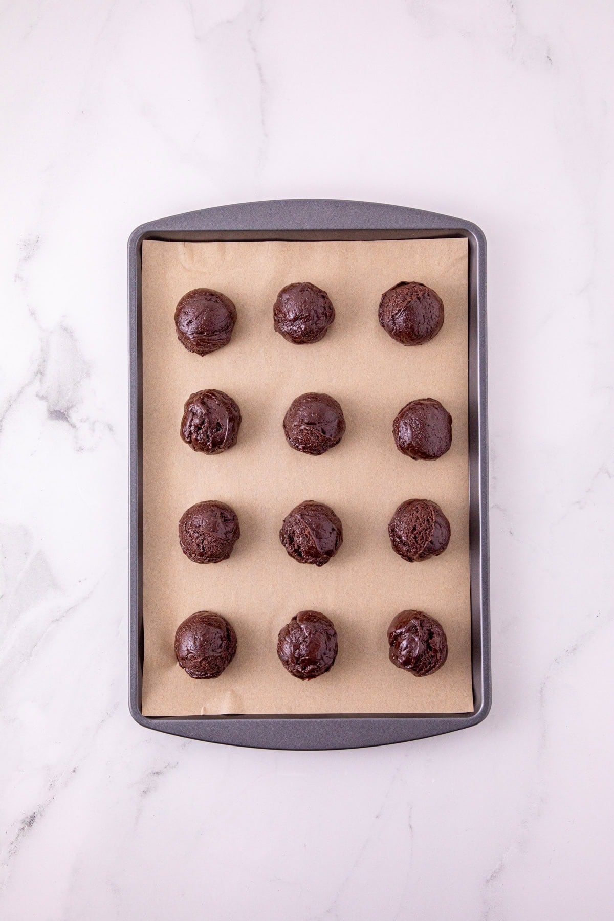 Scoops of chocolate cookie dough arranged on a parchment-lined baking sheet.
