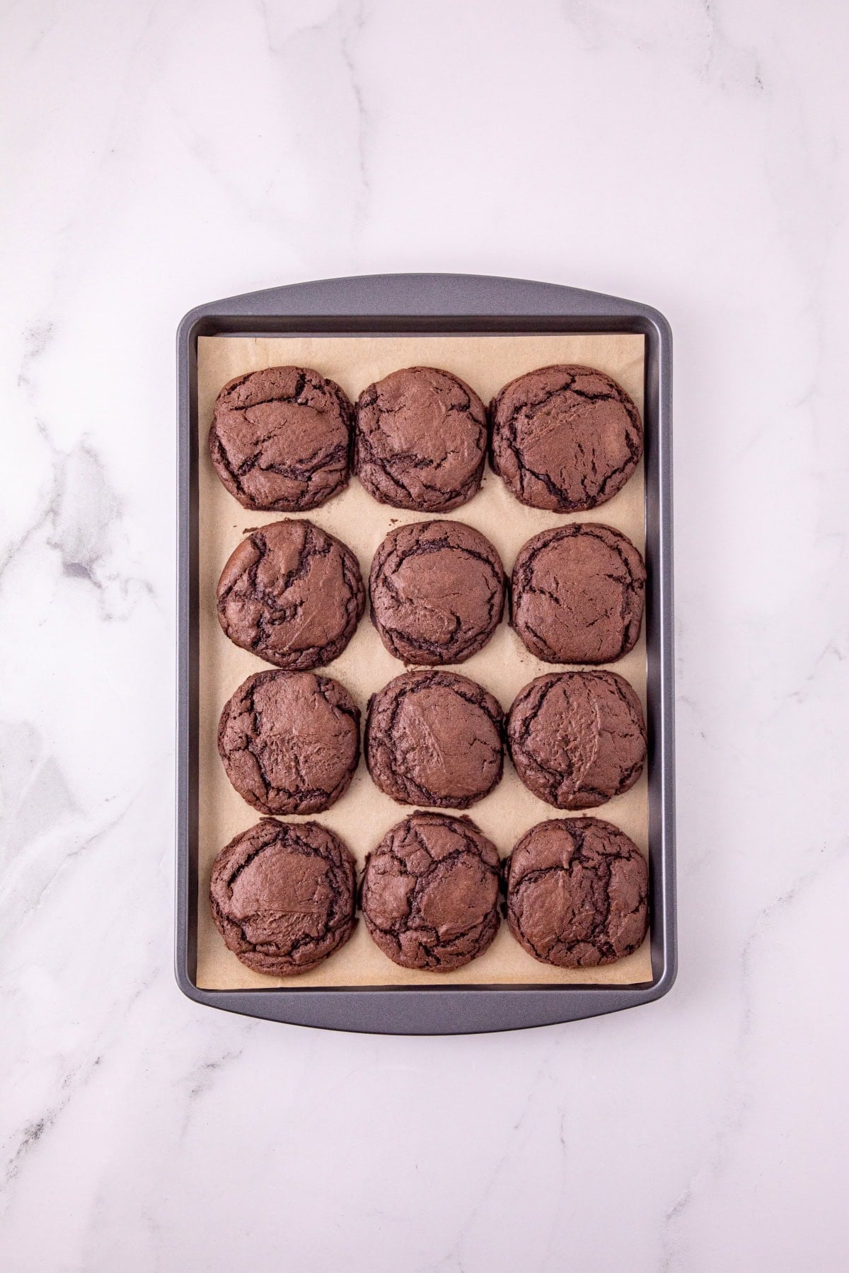 Freshly baked chocolate cake mix cookies cooling on a parchment-lined baking sheet.