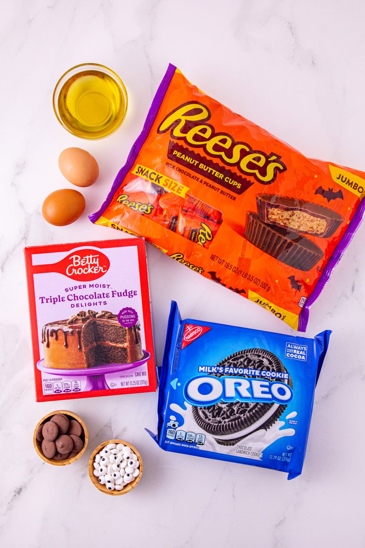 Ingredients for Oreo bat cookies, including chocolate cake mix, Reese’s peanut butter cups, Oreos, eggs, oil, chocolate melts, and candy eyes.