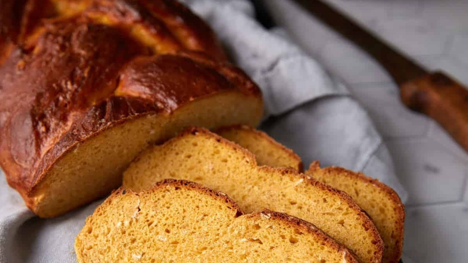 A golden-brown braided sweet potato yeast loaf partially sliced into soft, yellow-orange rounds on a cloth towel.