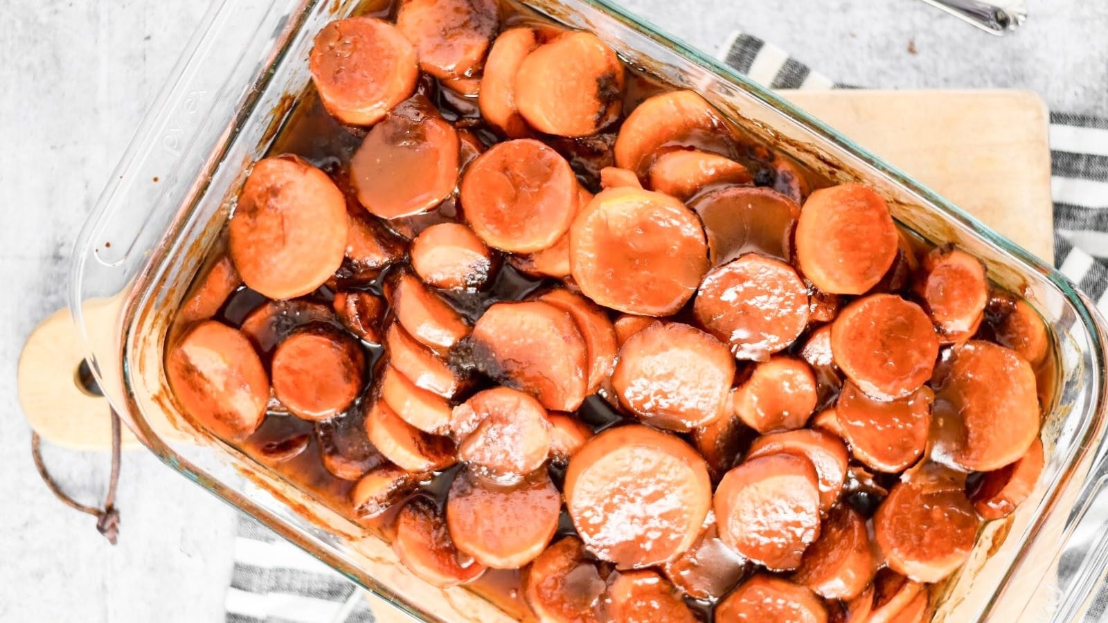 Sliced sweet potato rounds coated in a glossy brown sugar syrup glaze inside a rectangular glass baking dish.