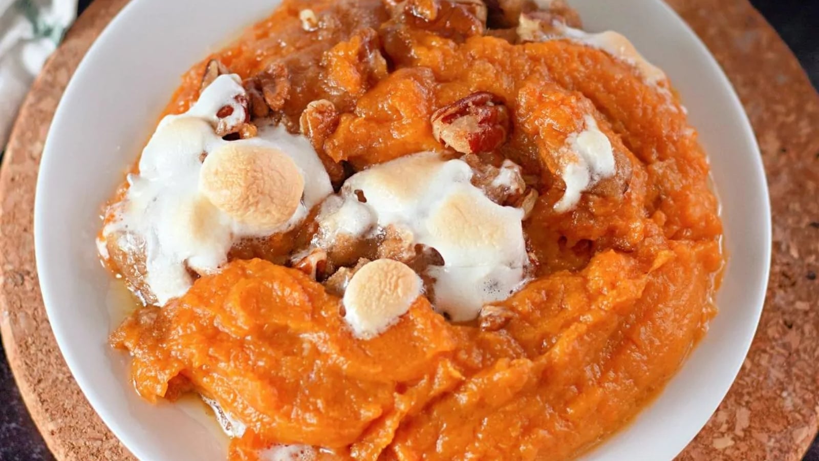 A plate of creamy mashed sweet potato casserole topped with toasted pecans and melted toasted marshmallows.
