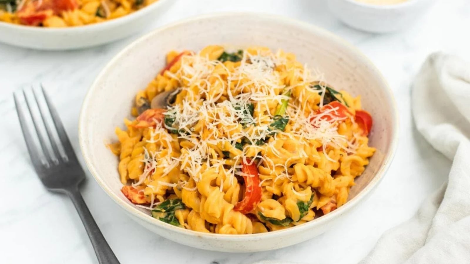 A bowl of fusilli pasta tossed in a creamy sweet potato sauce with spinach, red peppers, and shredded Parmesan cheese.