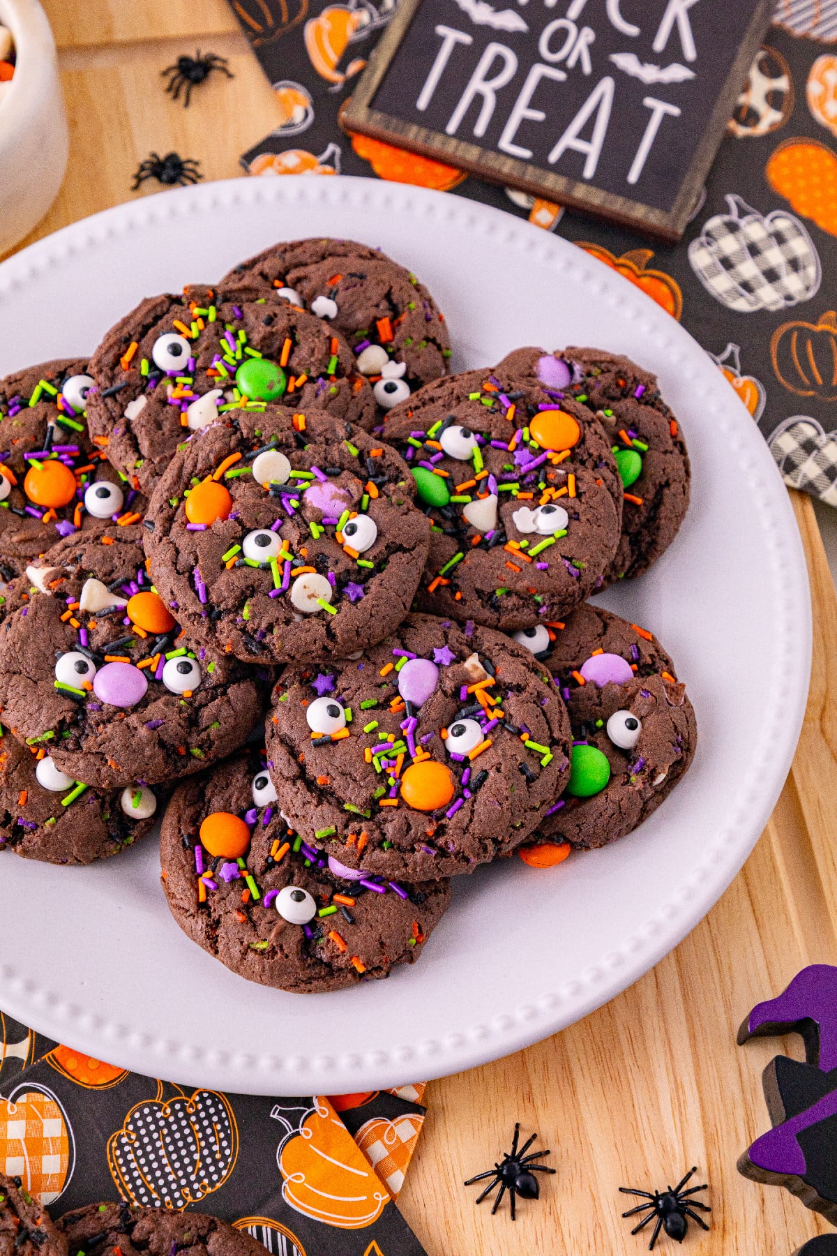 Chocolate Halloween cake mix cookies topped with colorful sprinkles, candy eyes, and orange and green candies on a white plate.
