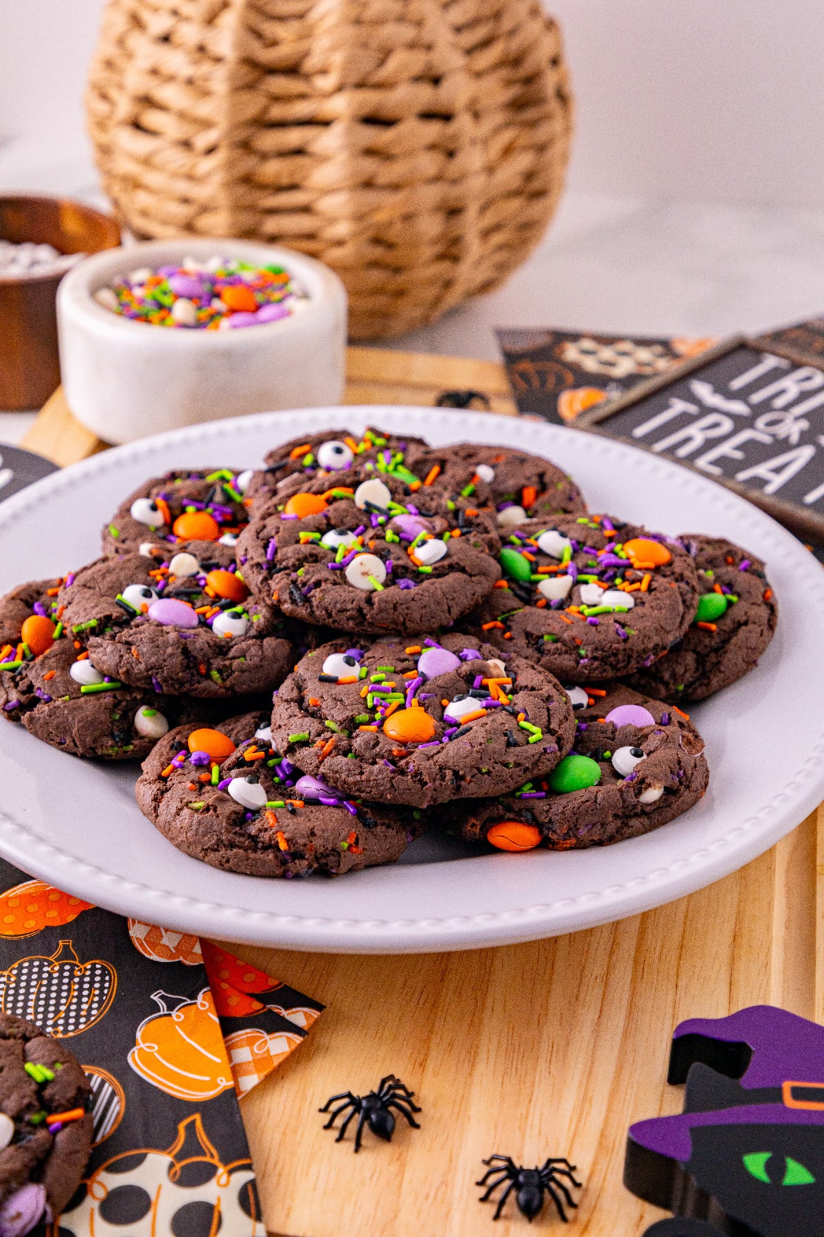 Chocolate Halloween cake mix cookies topped with colorful candies, sprinkles, and candy eyes on a white plate with Halloween decorations.