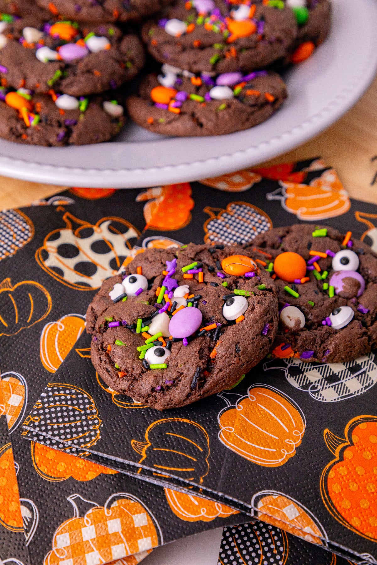 Chocolate Halloween cake mix cookies decorated with candy eyes, colorful sprinkles, and candies on a black and orange pumpkin-patterned napkin.