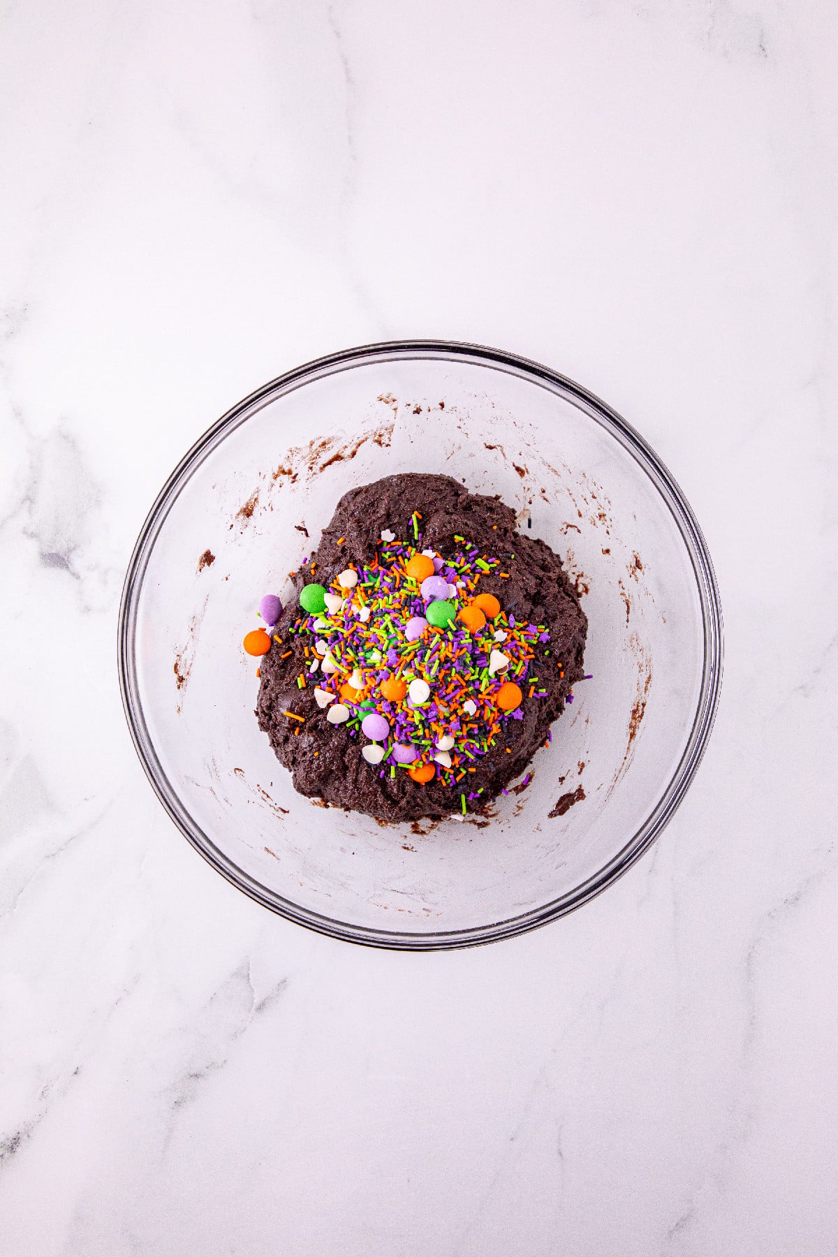 Chocolate cookie dough topped with Halloween baking confetti in a glass bowl.