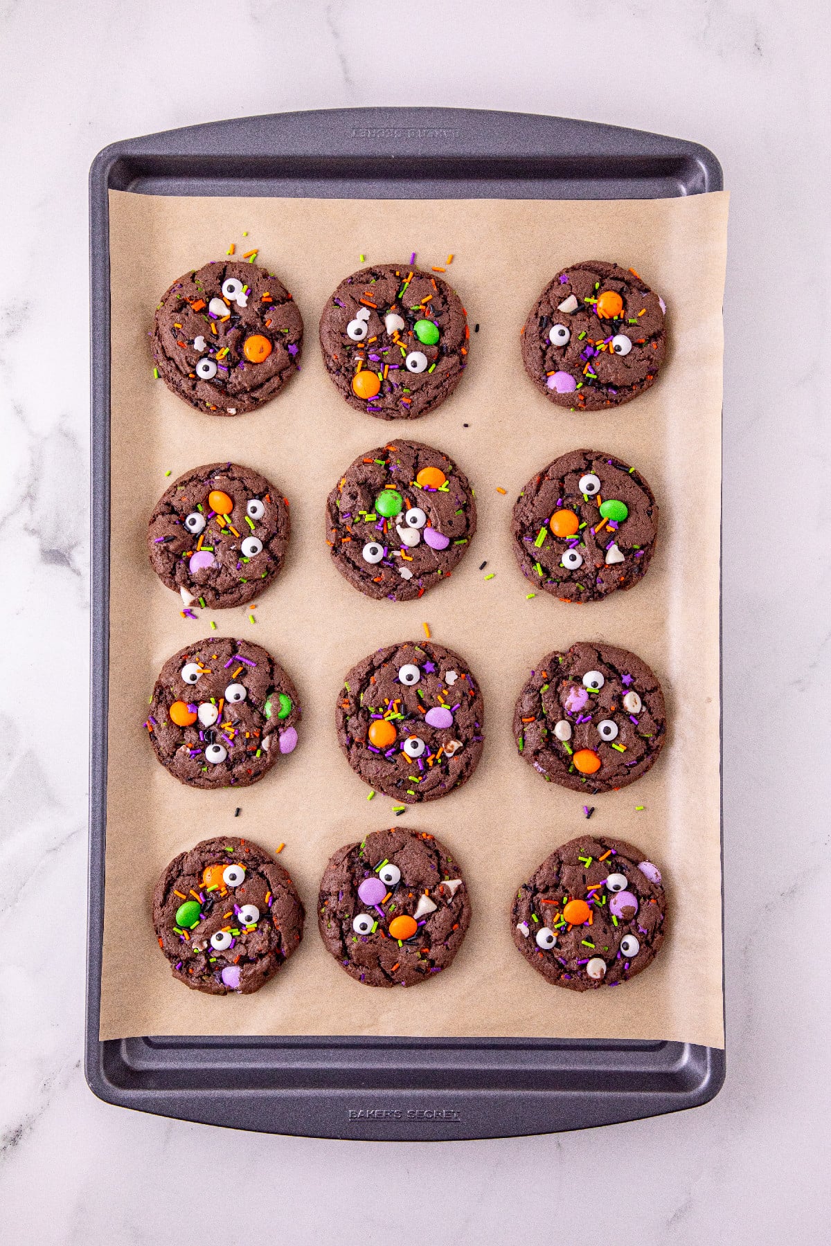 Baked Halloween cake mix cookies topped with candy eyes and colorful sprinkles on a baking sheet.