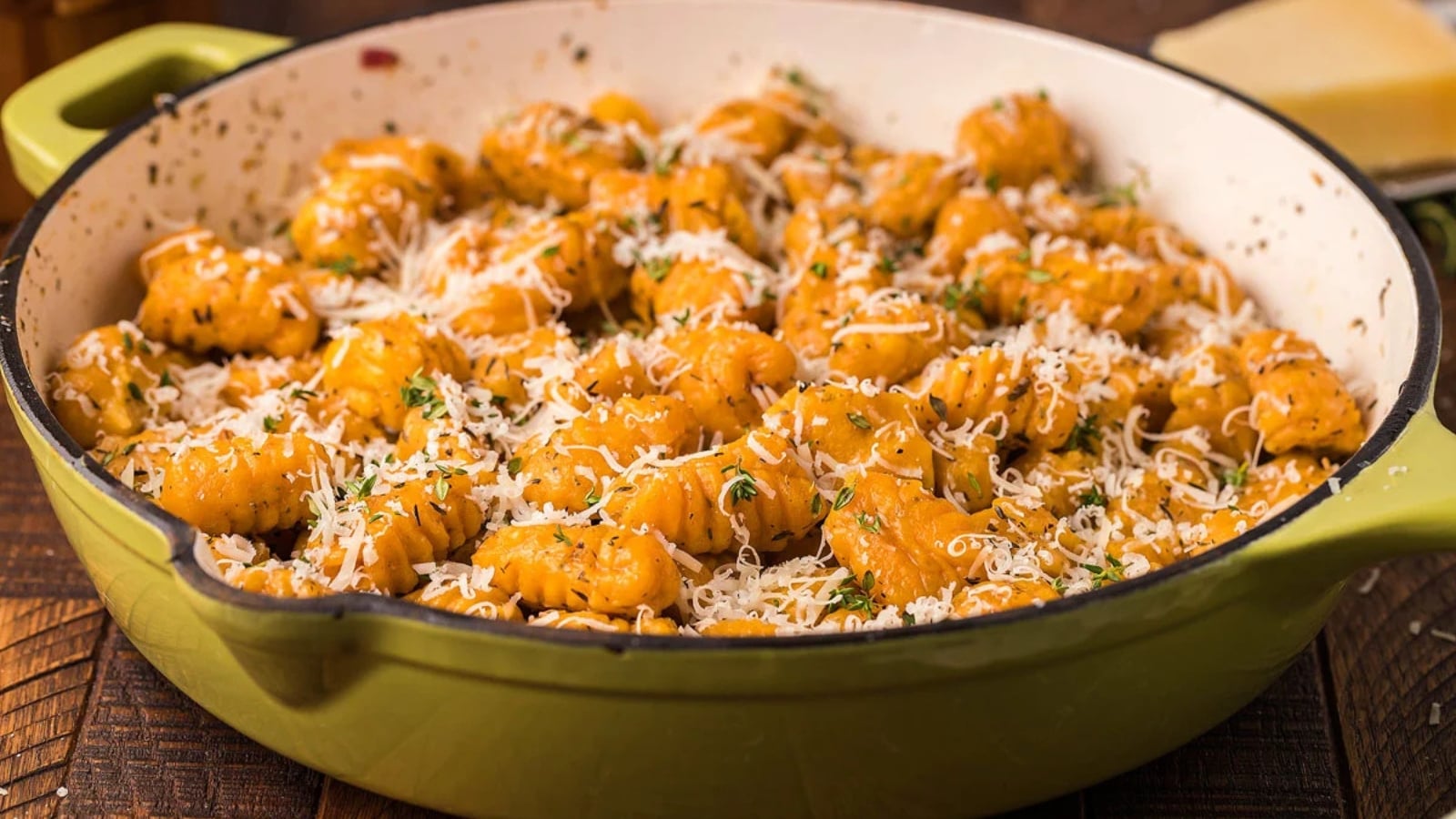 Handmade sweet potato gnocchi tossed in butter, topped with shredded Parmesan cheese and fresh thyme leaves in a green skillet.