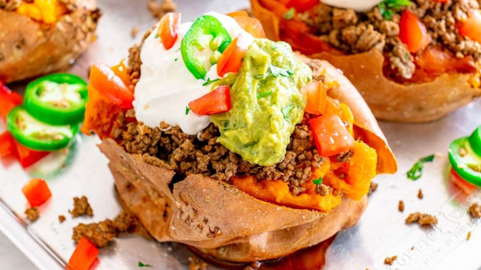 Baked sweet potato stuffed with seasoned ground beef and topped with sour cream, guacamole, diced tomatoes, and sliced jalapeños.