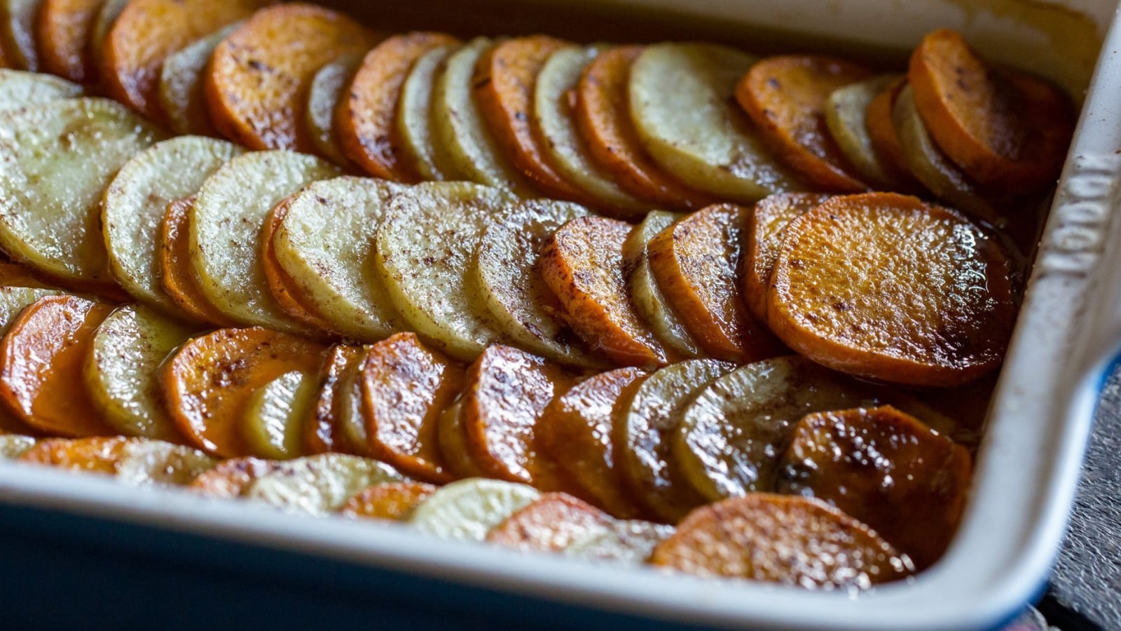 Thinly sliced orange and white sweet potatoes layered in rows inside a baking dish.