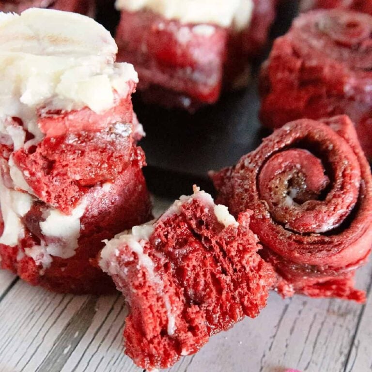 Red velvet cinnamon rolls topped with cream cheese frosting, showing soft red swirls and a fluffy texture.